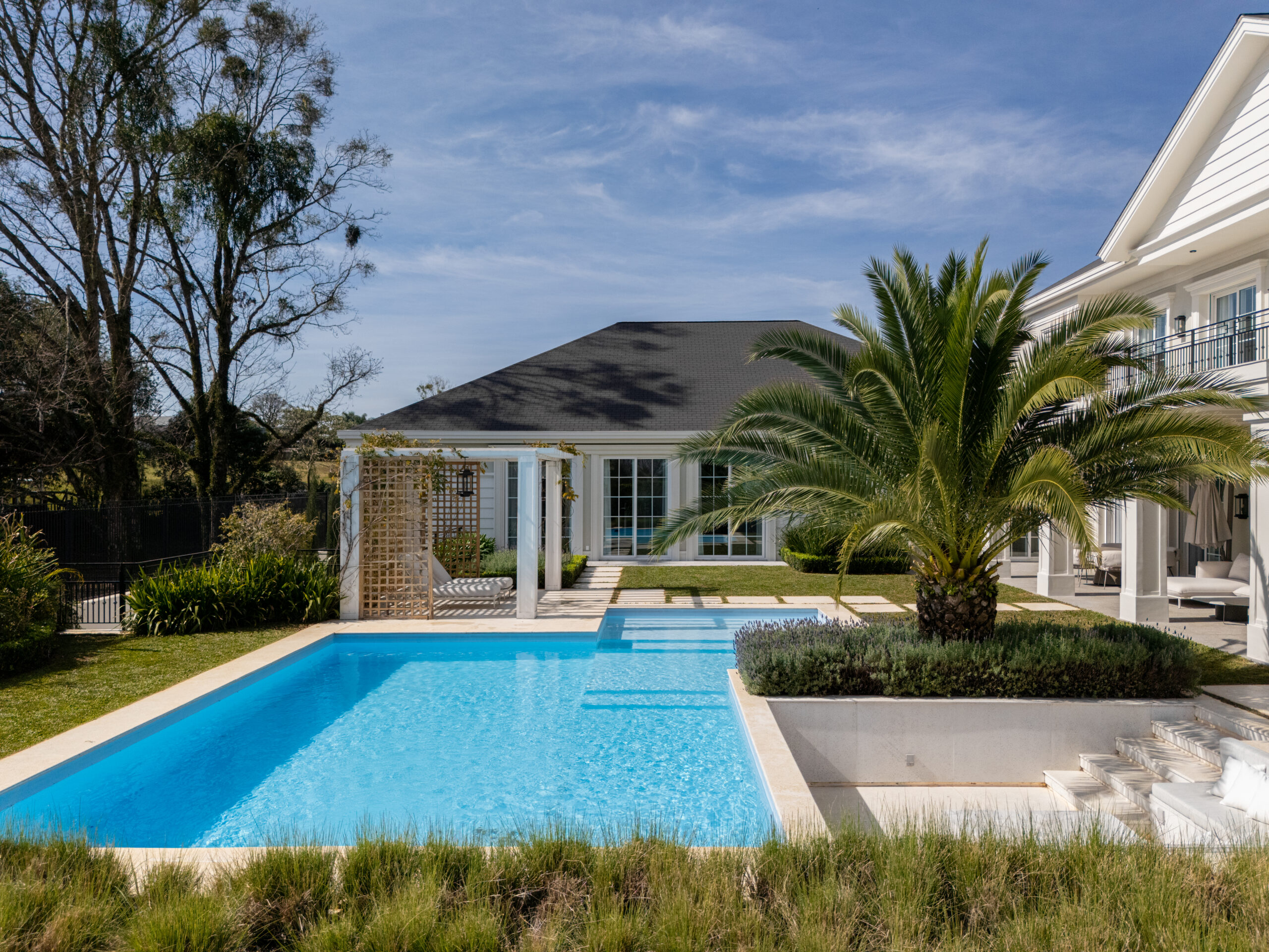 Um projeto de piscina moderno localizada em uma mansão, cercada por um jardim bonito