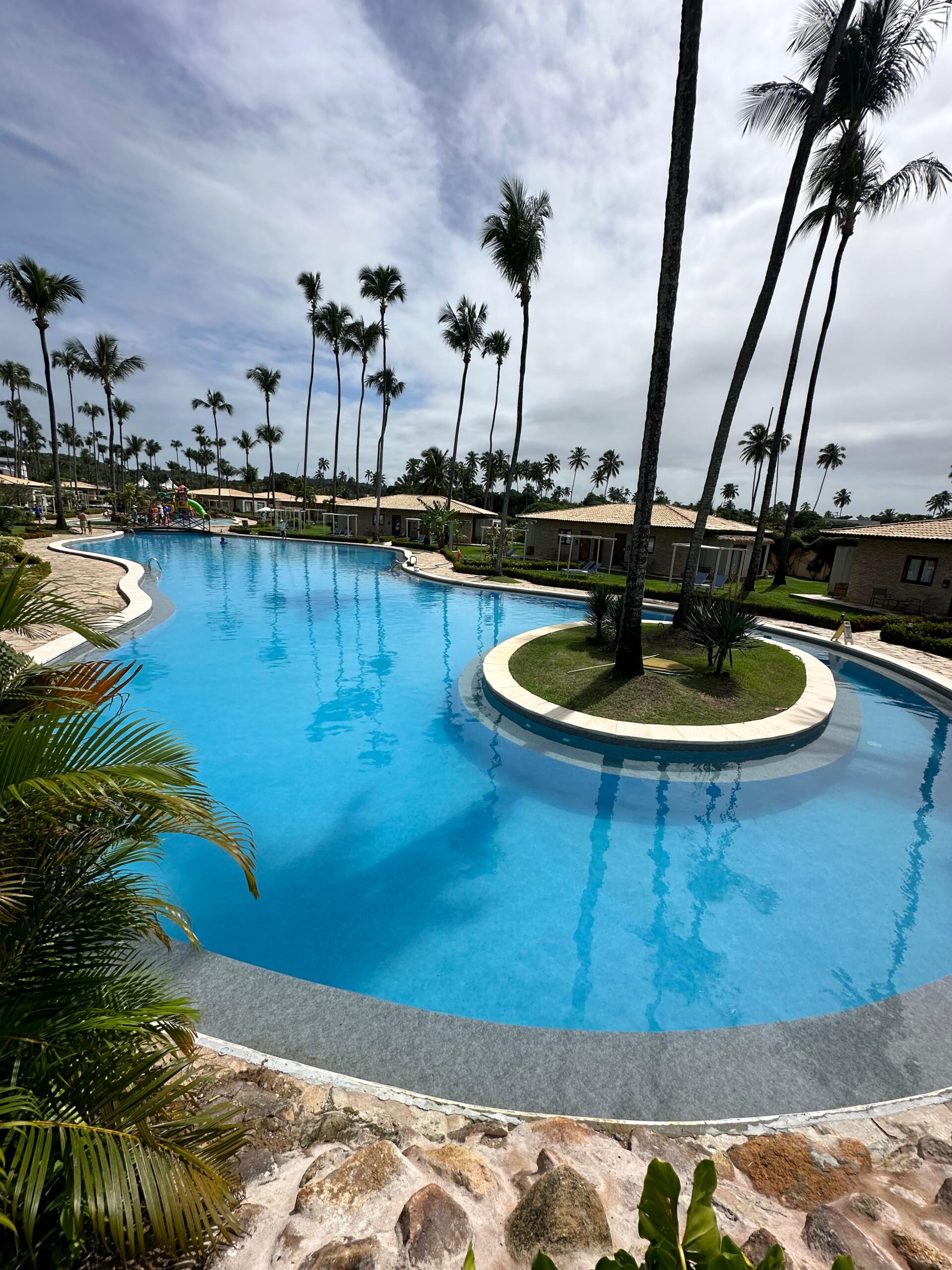 Uma piscina coletiva com árvores e pequenas casas ao redor localizada em um Resort no Nordeste